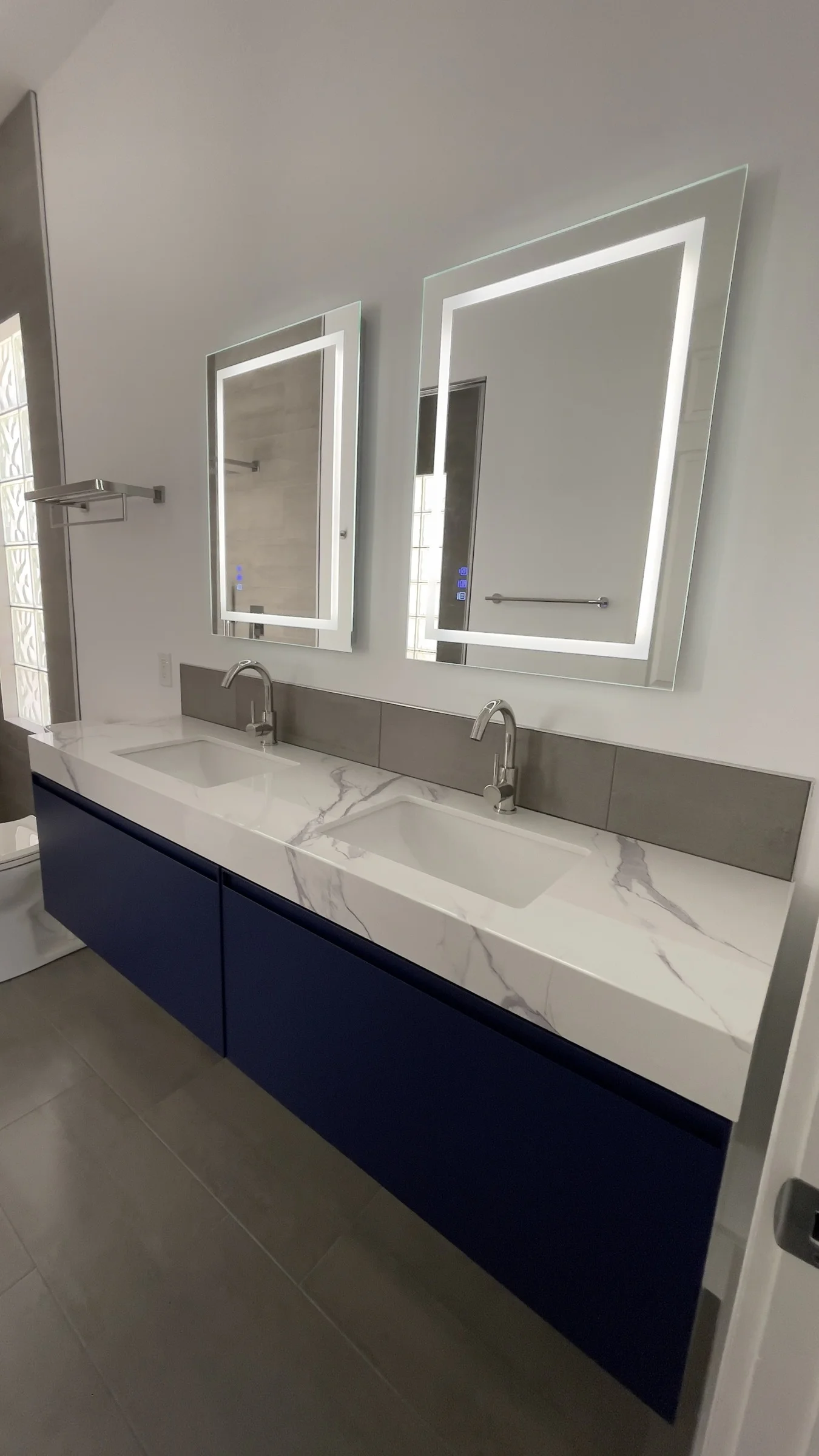 Blue floating double vanity with a white stone countertop and two illuminated mirrors