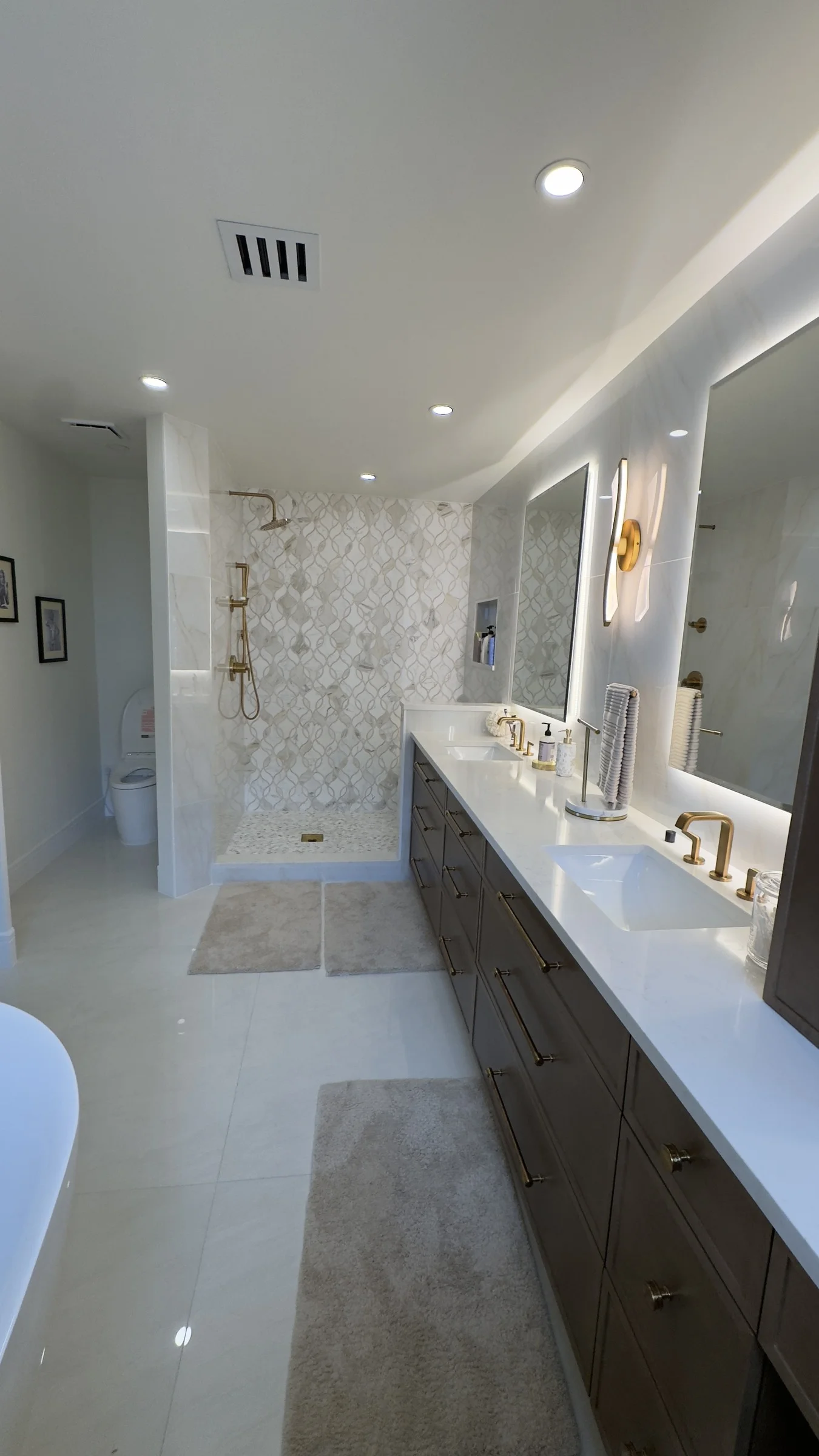 Bright finished bathroom with a double vanity, patterned walk-in shower, and brass fixtures