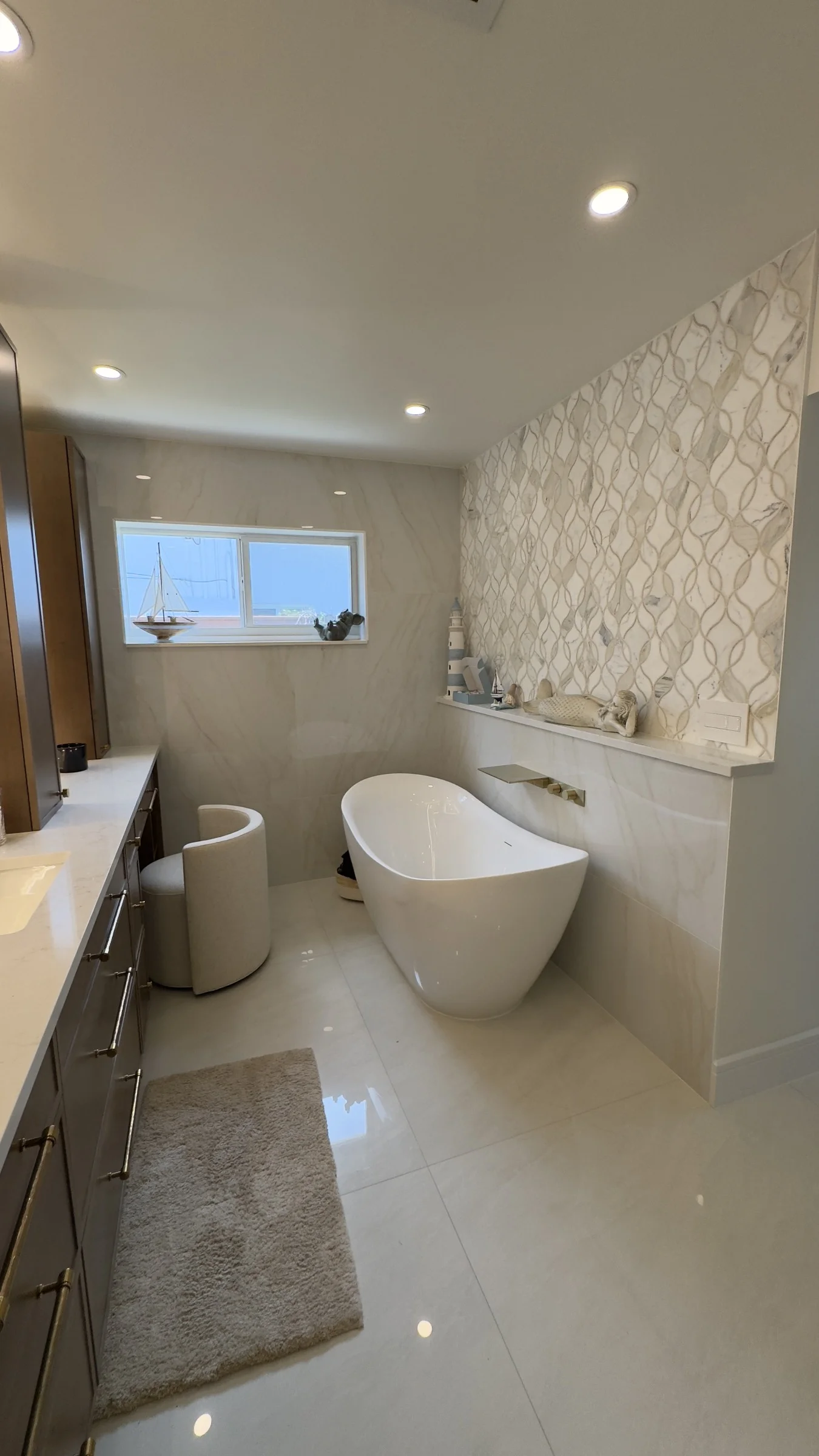 Freestanding white bathtub beside a patterned tile feature wall in a finished bathroom