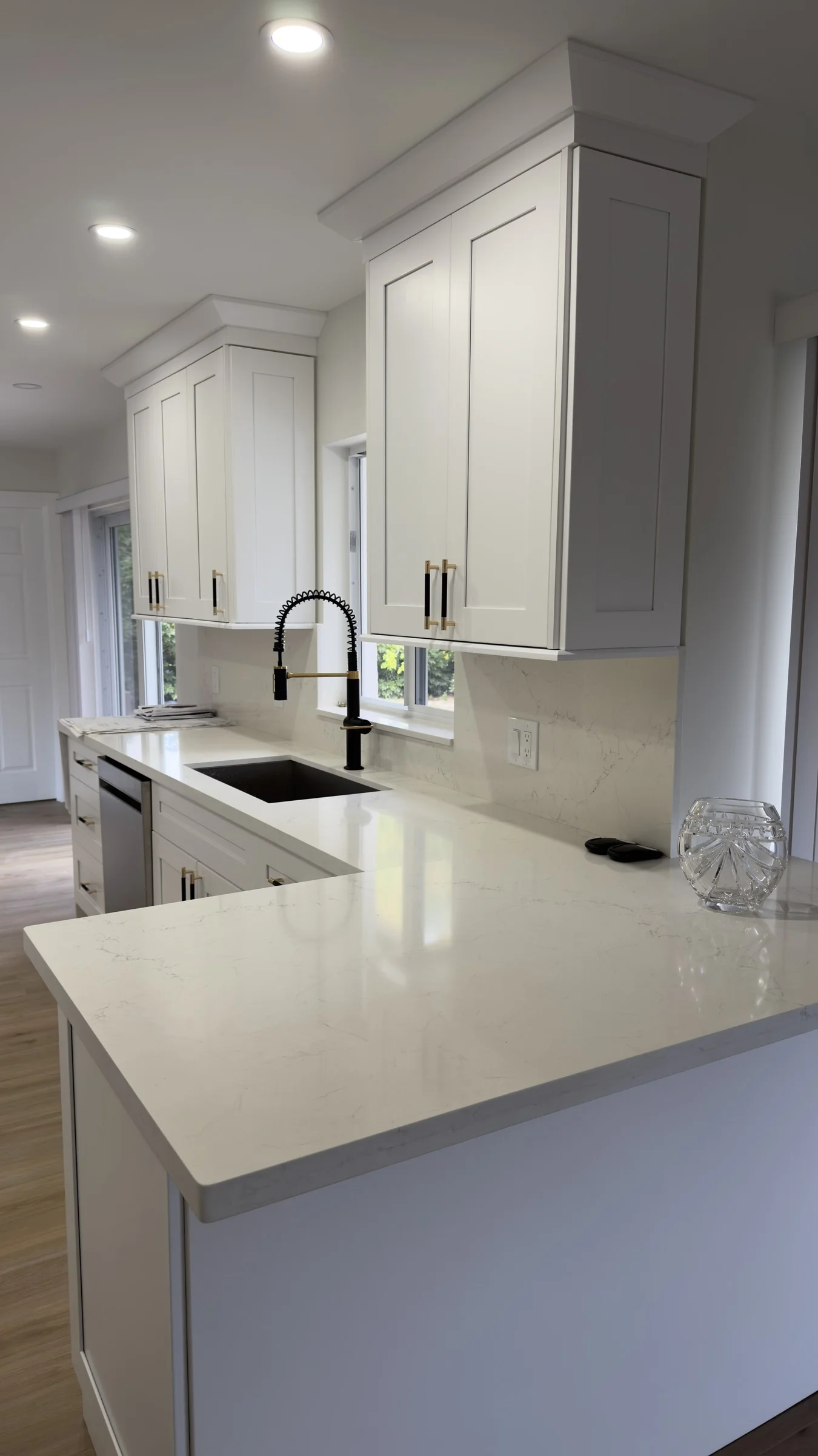 Finished kitchen with white shaker cabinets, white counters, a black and brass faucet, and wood flooring