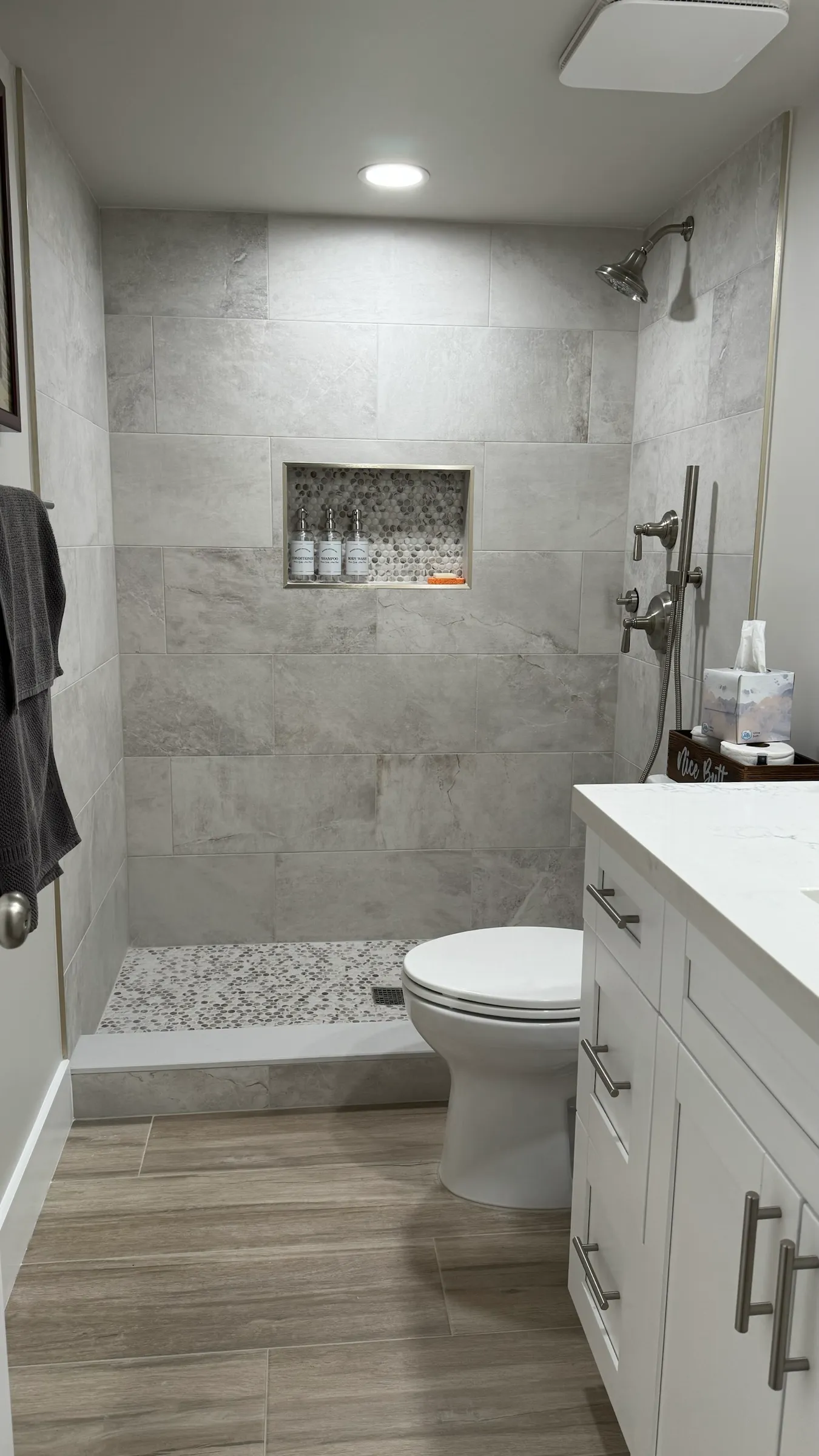 The same bathroom after remodeling, with a tiled walk-in shower, recessed niche, handheld shower and updated vanity.